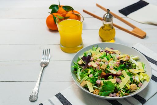 A plate of fresh Mediterranean salad with olive oil served with orange juice on a white wooden table