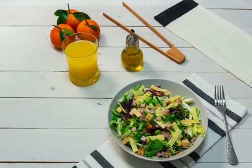 A plate of fresh Mediterranean salad served with olive oil and orange juice on a white wooden table
