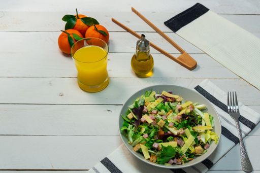 A plate of fresh Mediterranean salad served with olive oil and orange juice on a white wooden table