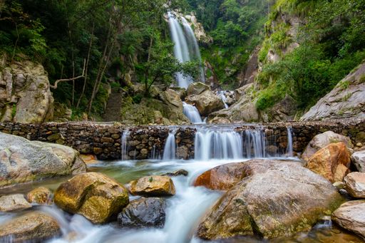 A mesmerizing view of small waterfalls flowing to the rocky river surrounded by green trees