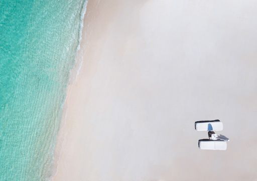 An aerial view of a beach with lounge chairs washed by blue ocean waves