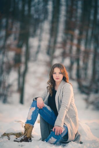 A shallow focus of a young female sitting on the ground in a forest covered in the snow