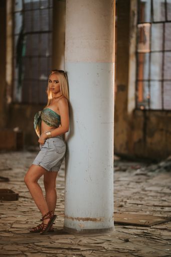 A shallow focus of a sexy confident blonde female wearing shorts with a crop top and posing against a column