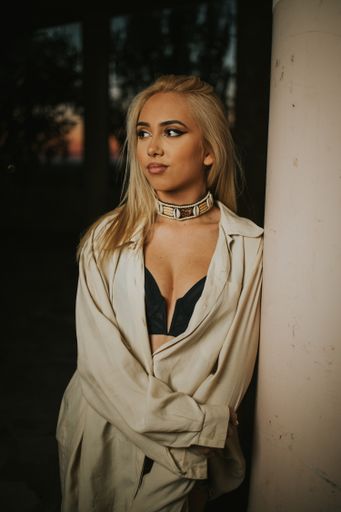 A shallow focus of a young blonde woman wearing a loose shirt and leaning on a wall at night