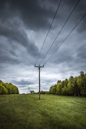 A vertical shot of a power line on a meadow under a cloudy sky