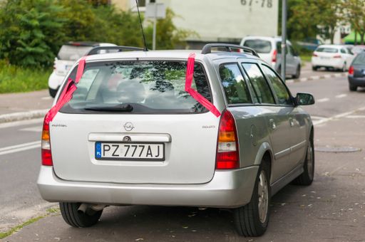 Gray Opel Astra stationcar with a new back window secured with red tape parked on a sidewalk.