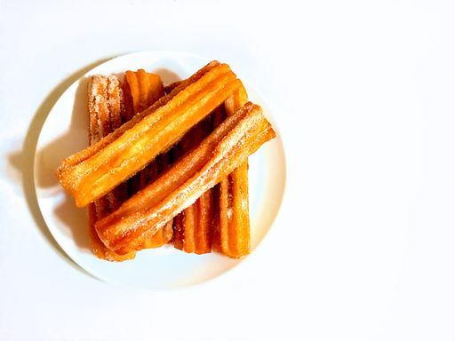 sweet sugared churros, traditional Argentine fried dough pastry of Spanish origin, on plate isolated on white background. Overhead shot. Copyspace
