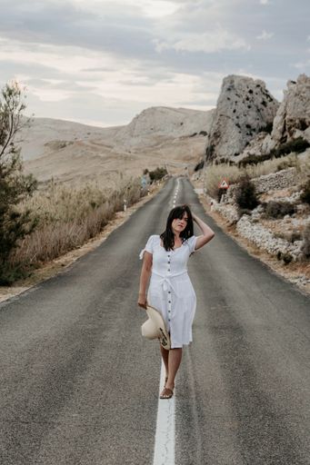 An attractive Croatian woman with a white dress on the road through a mountain valley during sunset