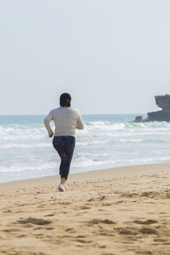 Mature woman with a black cap exercising at the beach on an out of focus sea background. Selective focus. Healthy lifestyle and running concept.