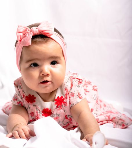 A vertical shot of a Spanish kid with pink dress and headband on white background