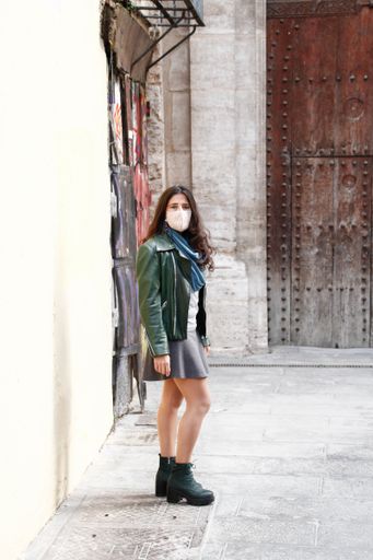 A vertical shot of a young Hispanic female wearing a medical mask posing outdoors