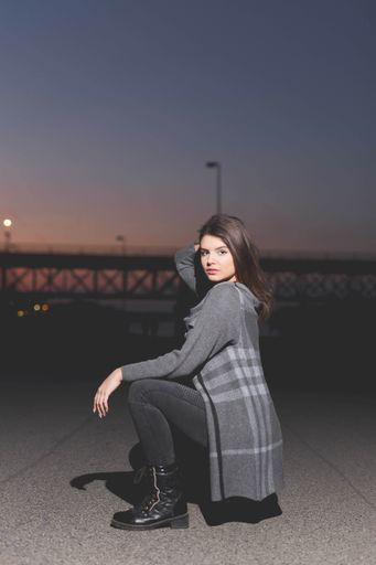 A vertical shot of a hot Caucasian woman posing on the road in a grey and black outfit with boots