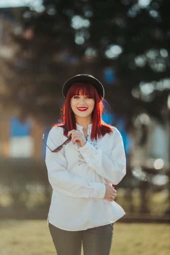 A vertical shot of a beautiful caucasian woman with red hair posing in a park during daylight
