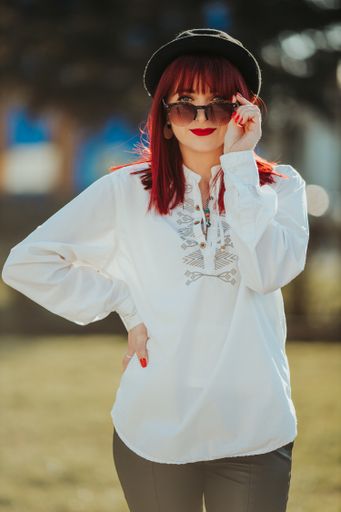 A vertical shot of a beautiful caucasian woman with red hair posing in a park during daylight