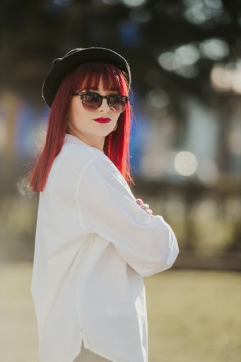 A vertical shot of a stylish caucasian female with red hair wearing a white shirt and hat