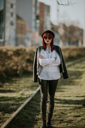 A sexy redhead with sunglasses and a black hat walking across railway with her arms crossed