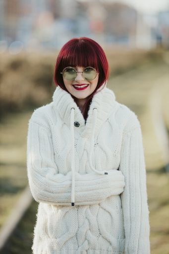 A vertical shot of a beautiful caucasian woman with red hair, wearing a white woven sweater in a park