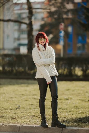 A vertical shot of a beautiful caucasian woman with red hair, wearing a white woven sweater in a park