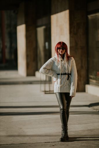 A vertical shot of a beautiful caucasian woman with red hair, wearing a white woven sweater in a park