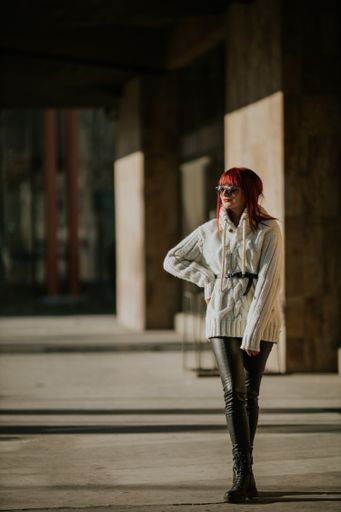 A vertical shot of a Caucasian red-haired woman standing on a blurred background