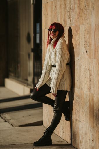 A vertical shot of a beautiful caucasian woman with red hair, wearing a white woven sweater in a park