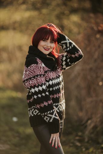 A vertical shot of a beautiful caucasian woman with red hair, wearing a woven sweater in a park