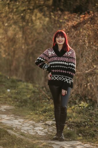 A vertical shot of a beautiful caucasian woman with red hair, wearing a woven sweater in a park