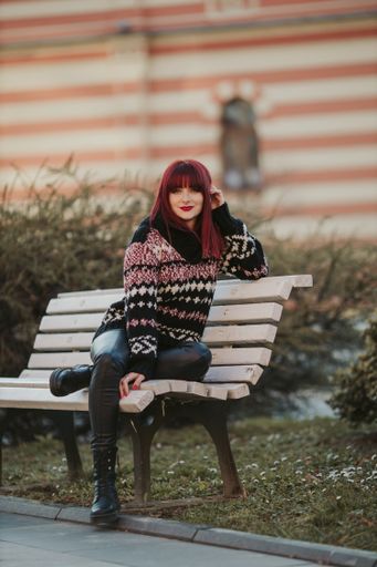 A vertical shot of a Caucasian red-haired woman sitting on a bench