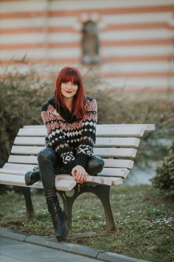 A vertical shot of a young caucasian female with red hair in a cozy sweater sitting on a bench