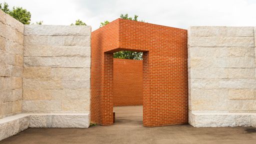 A photo of a space enclosed by red brick walls with an opening at the corner