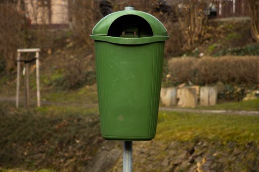 A green trash bin in a park
