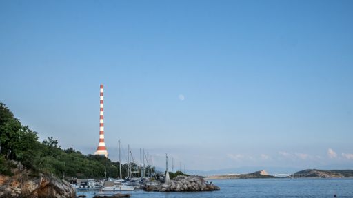 A view of boats and a large industrial chimney from the beach in Kostrena, Croatia