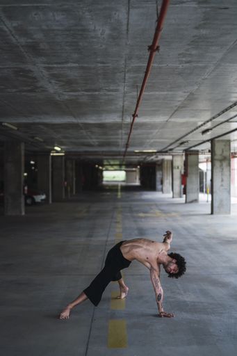 A vertical shot of a curly-haired topless man dancing in a parking lot in Spain