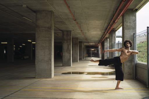 A shallow focus of a curly-haired topless man dancing in a parking lot in Spain