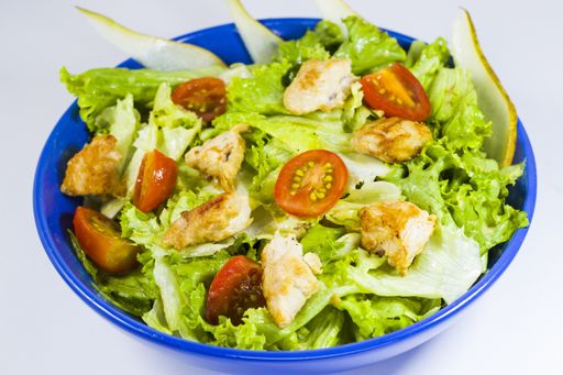 A closeup shot of chicken salad with greens, tomatoes, and apple in the blue bowl