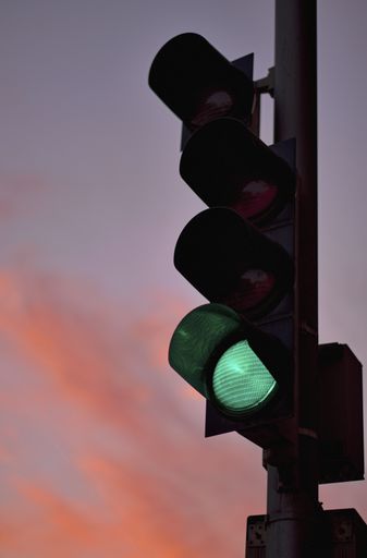 A vertical closeup shot of a traffic light with a green light on and a pink sky in the background