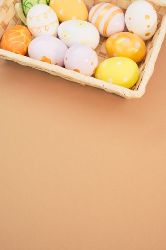 A vertical shot of woven basket with decorated Easter eggs on peach-colored background