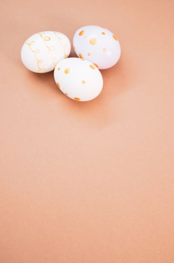 A vertical shot of decorated Easter eggs on peach-colored background