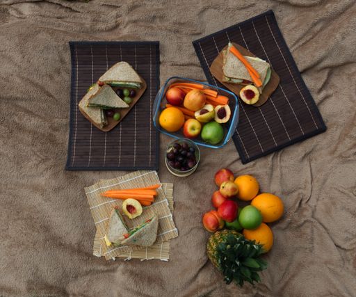 A top view of fruits and sandwiches for a picnic on a blanket