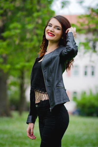 A shallow focus of a stylish young female wearing jeans with a crop top and leather jacket in a park