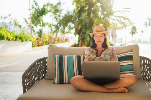 A beautiful shot of a Hispanic woman wearing a hat and working on her laptop sitting on a couch