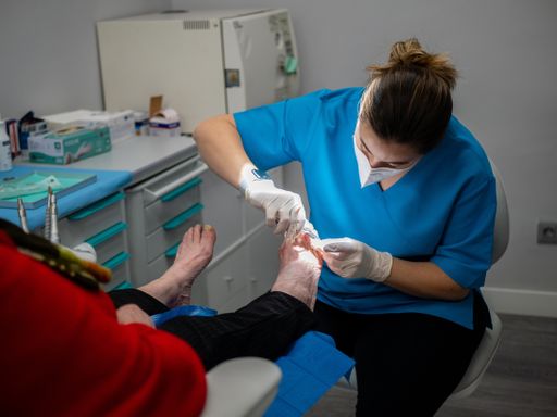 A female podiatrist in a medical mask and gloves treating the feet of a client