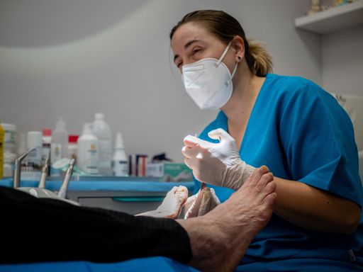 A female podiatrist in a medical mask and gloves treating the feet of a client