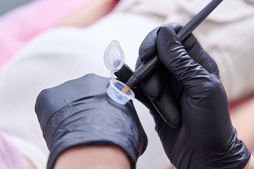 A beauty salon worker hands dunking the tool into the ink during microblading process