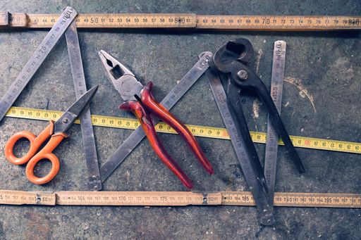A top view of pliers, scissors, rulers, and measuring tapes on a gray surface