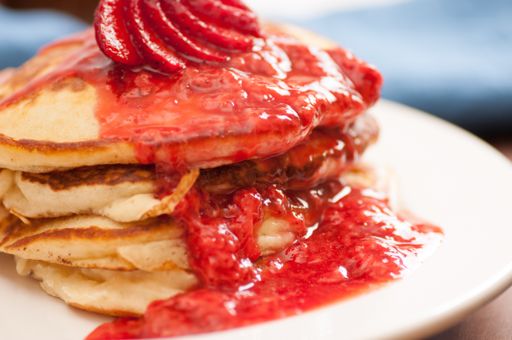 a stack of strawberry pancakes with butter, syrup and fresh berries