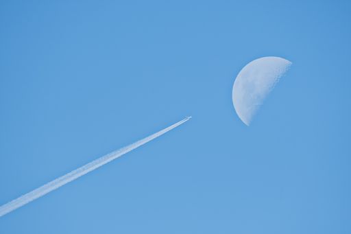 An airplane flying with a trail near the moon