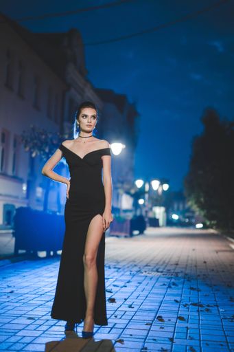A low angle shot of a confident Caucasian female in a black elegant dress posing for the camera