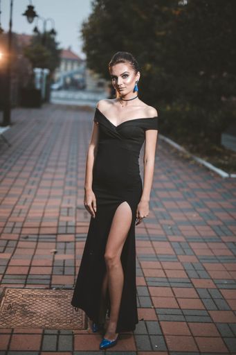 A shallow focus shot of a confident Caucasian female in a black elegant dress posing for the camera