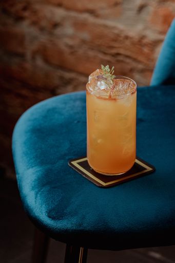 A cold refreshing cocktail in a glass on a light blue chair situated in the corner of a room